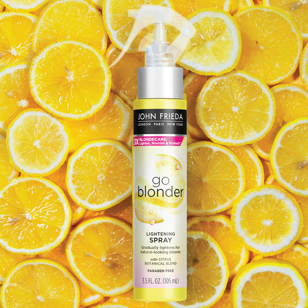A bottle of John Frieda Go Blonder® Lightening Spray surrounded by slices of lemons.