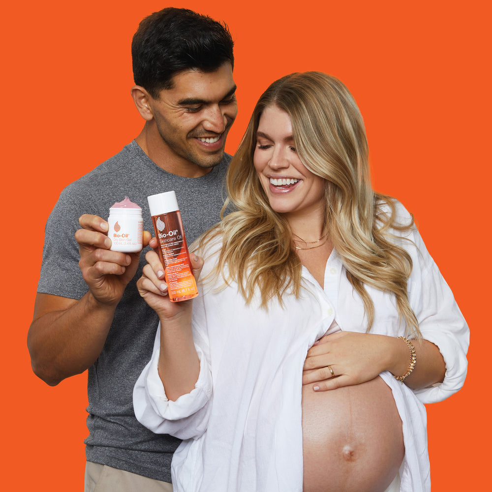A pregnant woman is holding a bottle of Bio-Oil Original 2 Month Bundle.